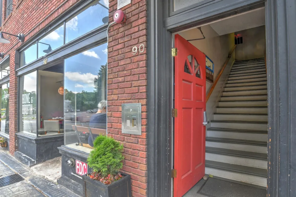 A welcoming brick building with a prominent red door and an inviting window display, suggesting a cozy café or boutique. People are seen visiting, socializing, and enjoying the local ambiance. The scene exudes warmth and friendliness, hinting at the local flavor and community connections present in the area.