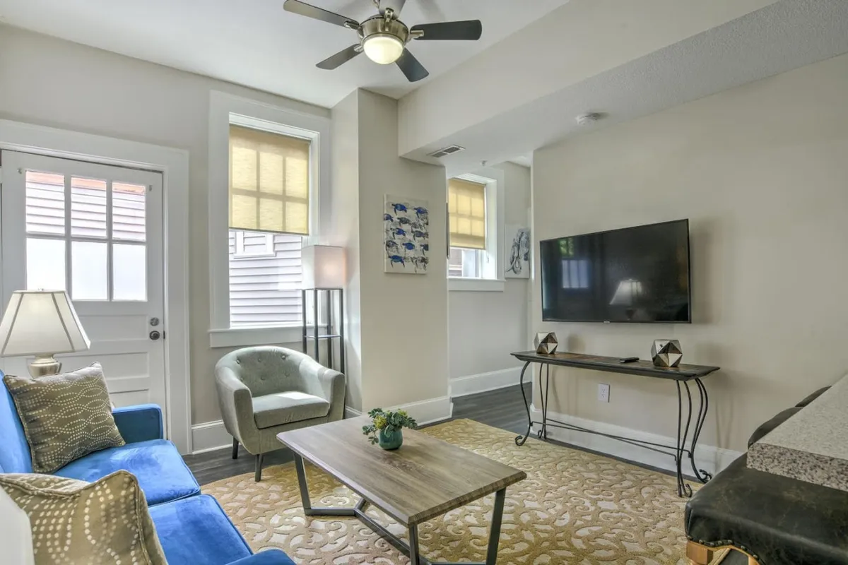 The image shows a stylish, inviting living area with a plush blue sofa, a sleek coffee table, decorative artwork, a warm lamp, and a TV, all arranged to maximize comfort and relaxation. The room exudes a cozy, welcoming atmosphere perfect for unwinding or spending quality time.